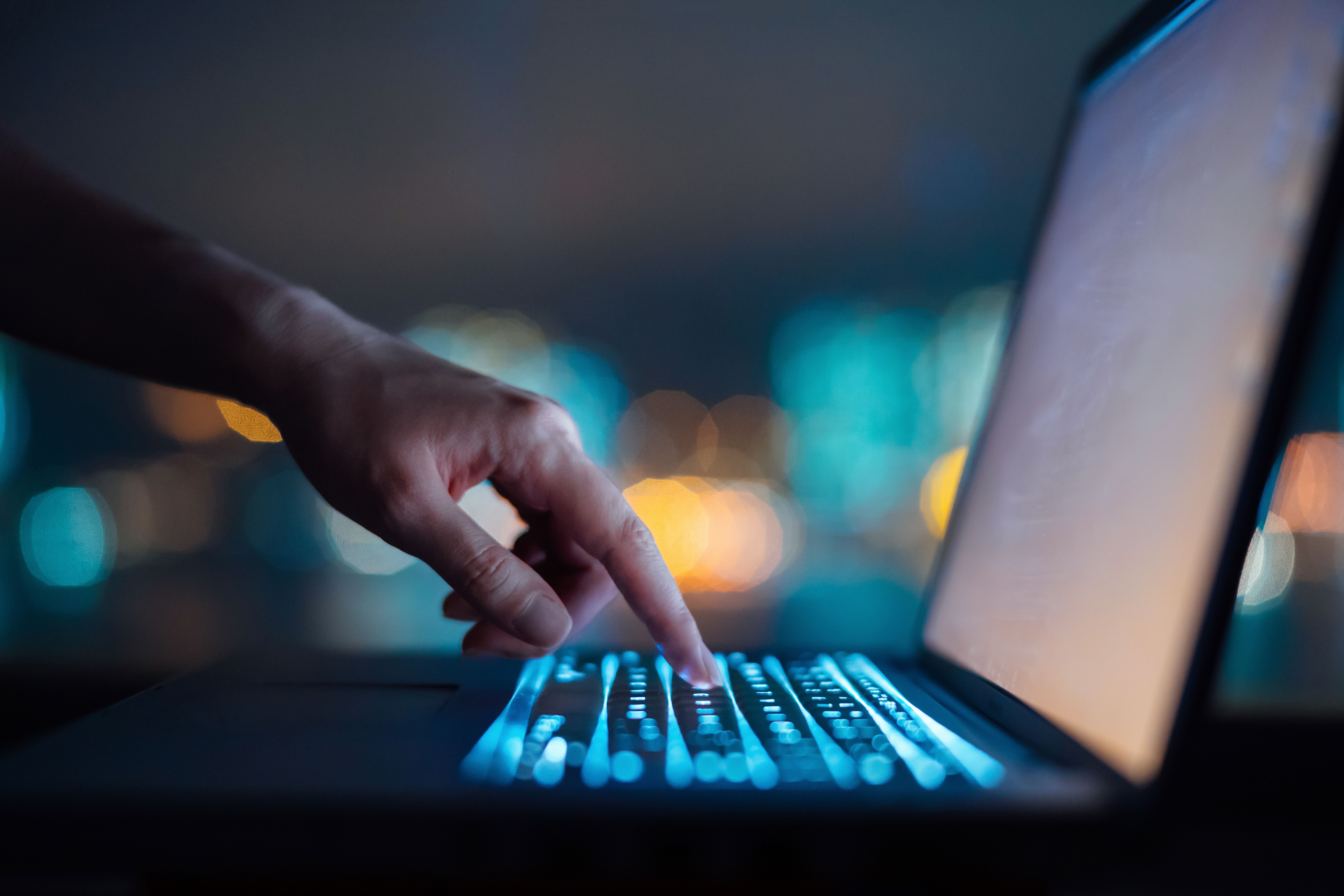 A hand pressing a lite up laptop in the dark