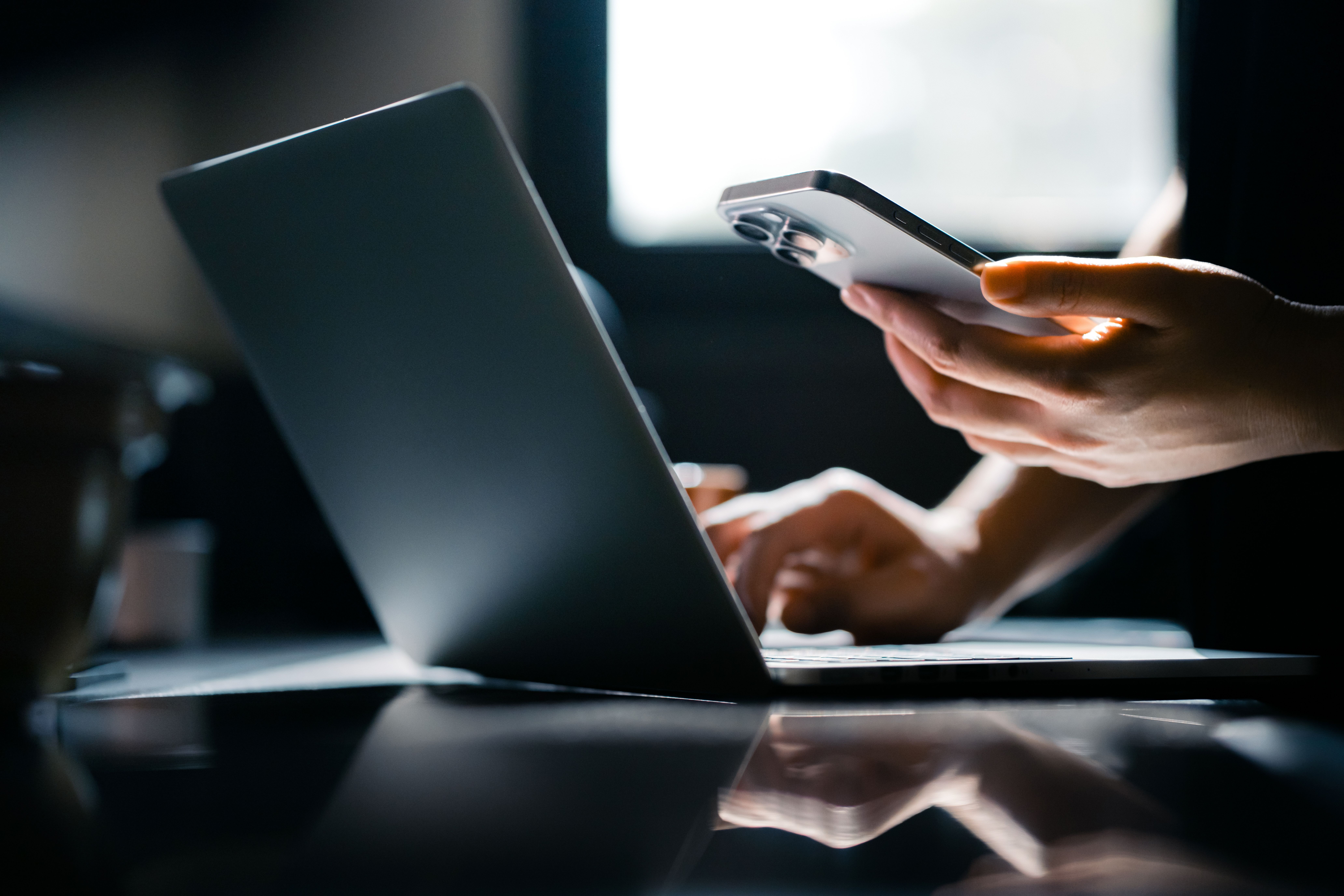 Person off screen holding an iphone while working on a laptop