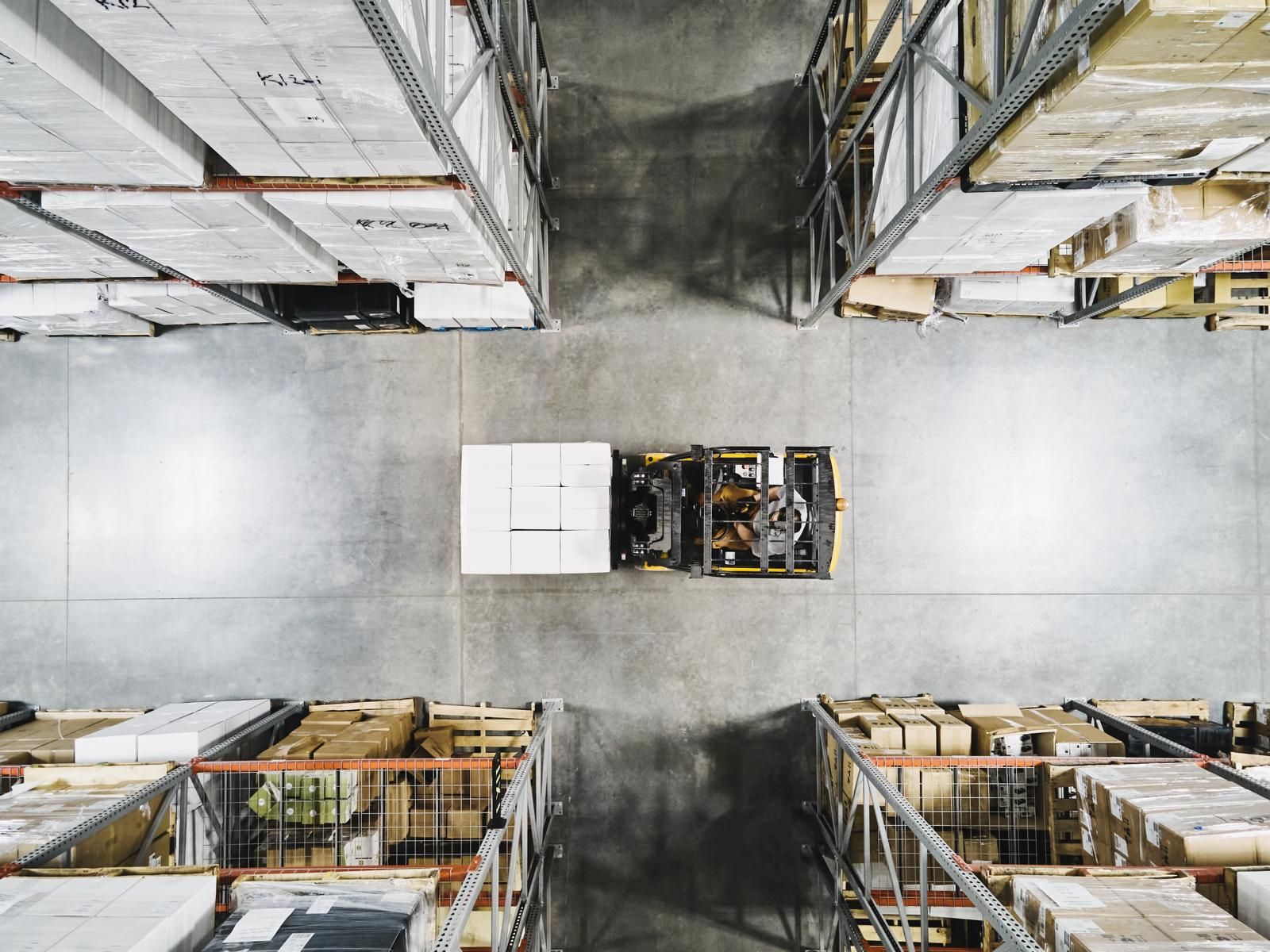 Overhead view of a yellow forklift moving a pallet down a warehouse aisle between loaded racking.