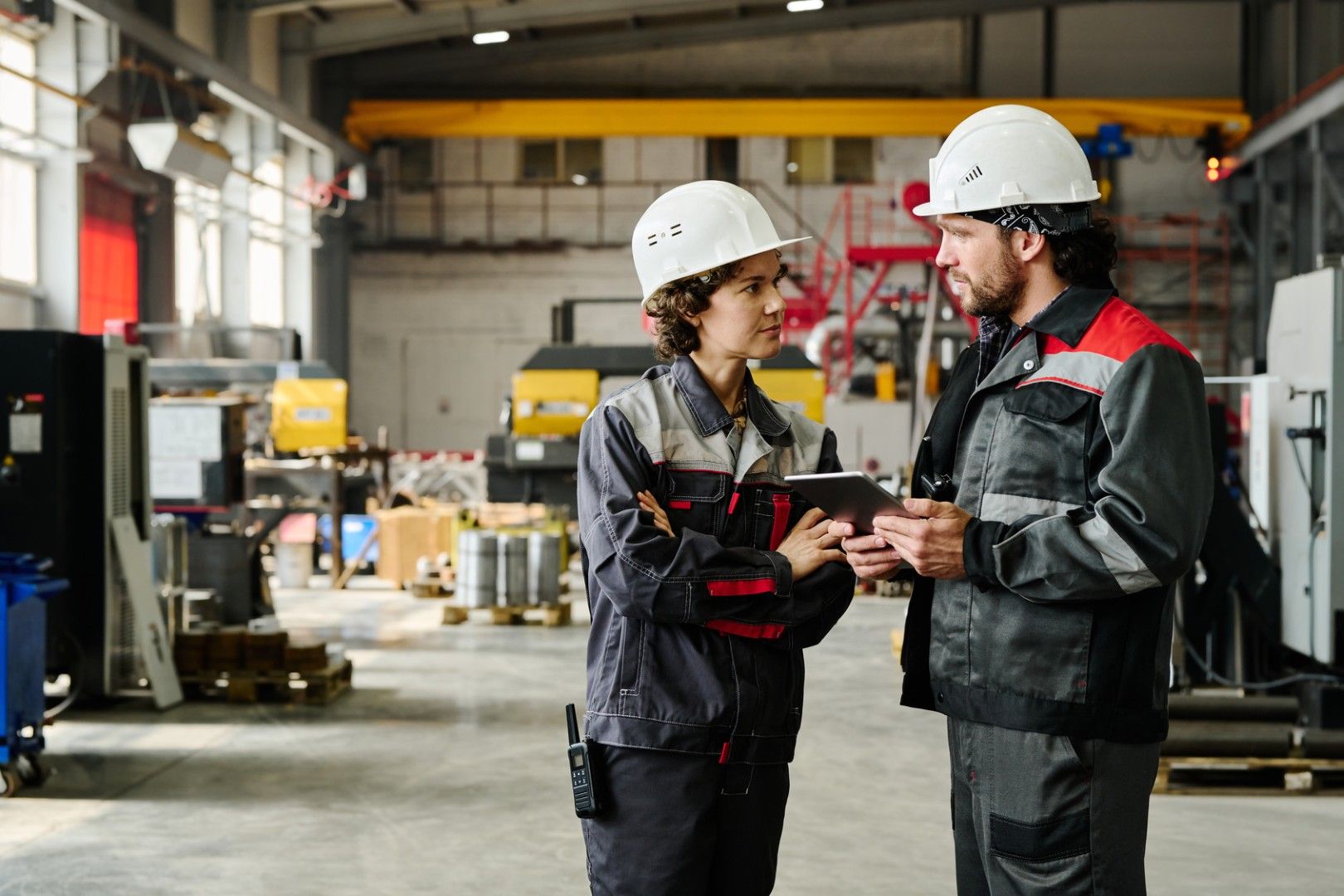 Two workers in branded workwear reviewing information on a tablet on a factory floor