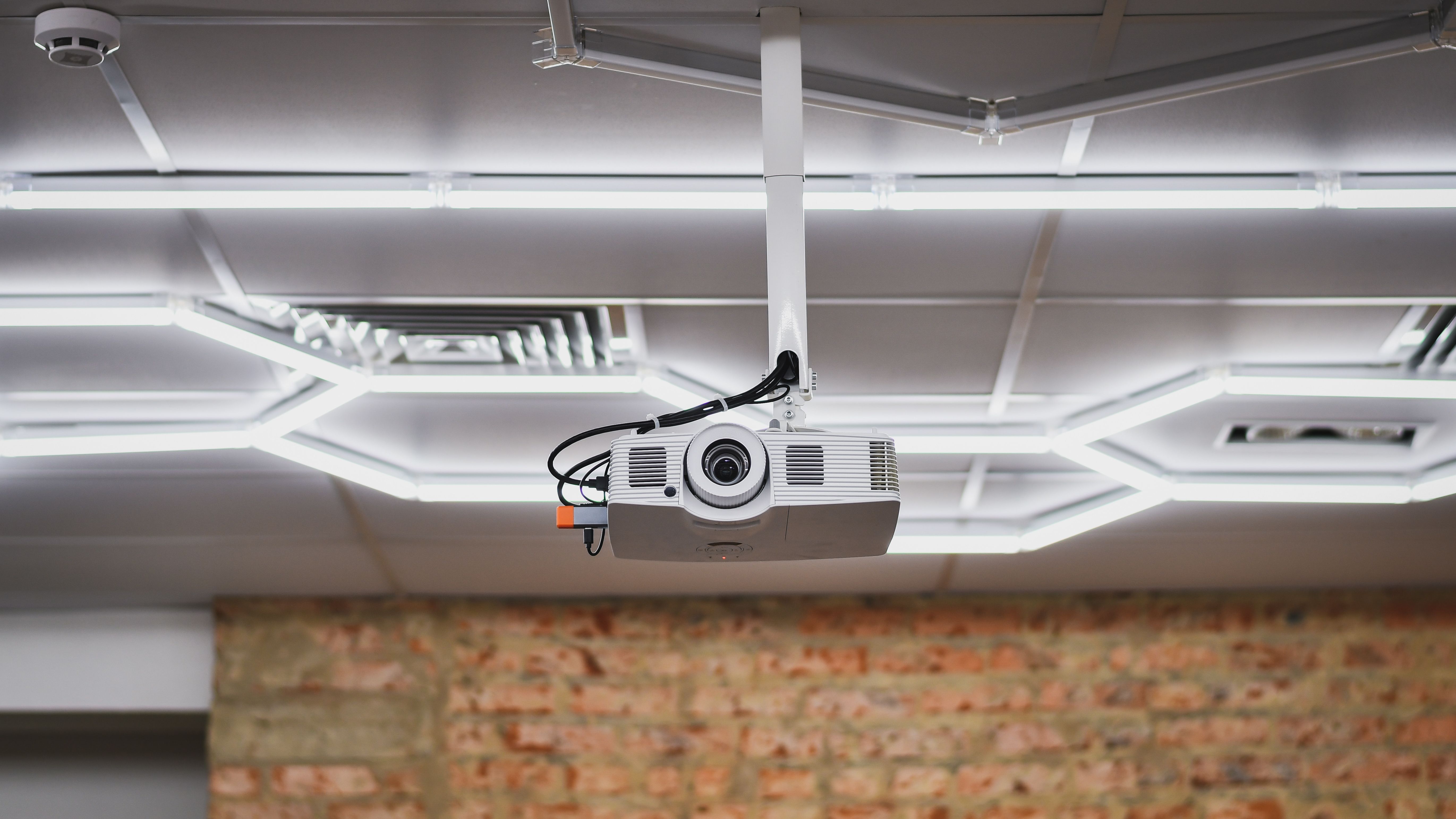 Ceiling-mounted projector in a modern office meeting room with a white ceiling and brick wall