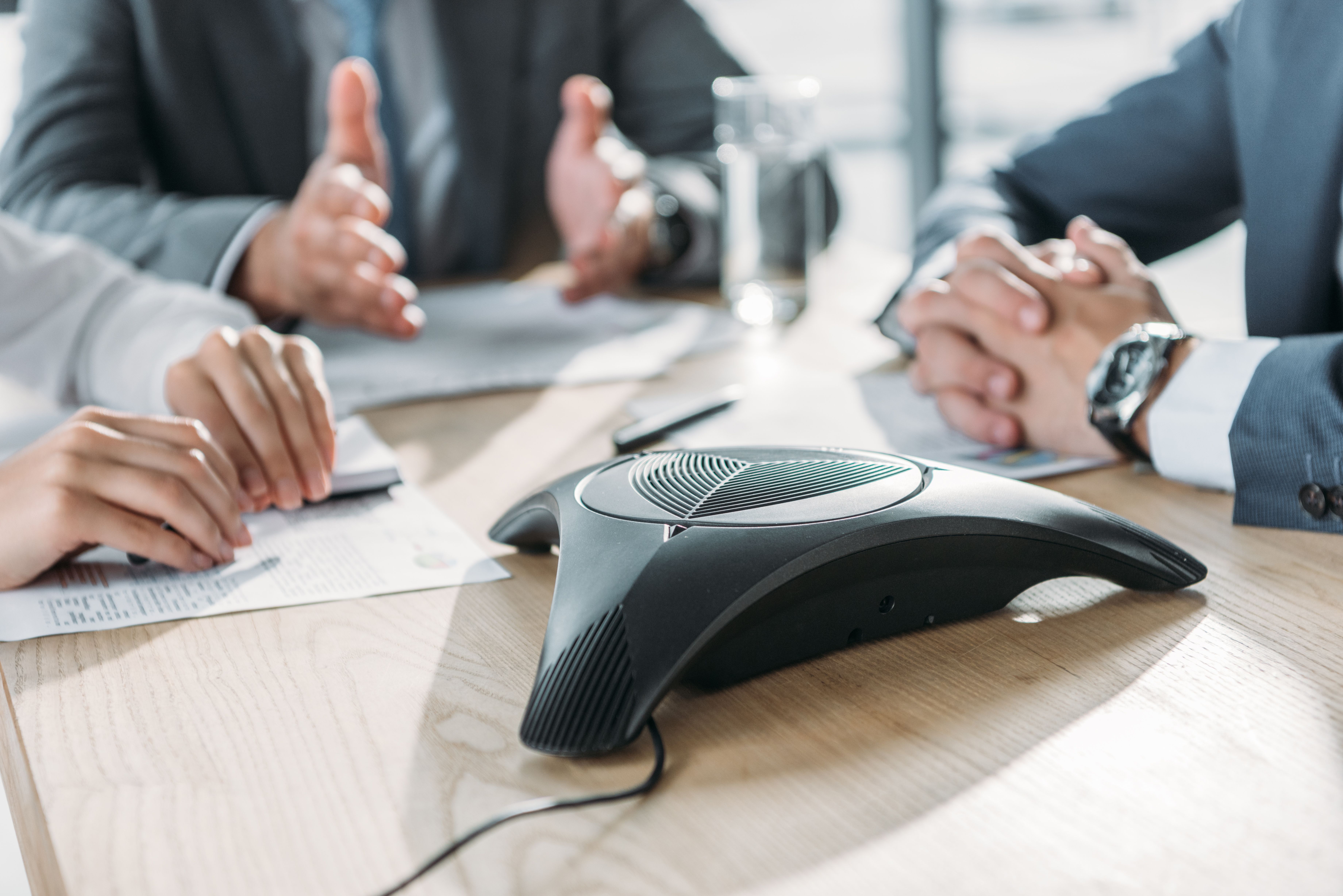 Conference speakerphone in the center of a wooden meeting table during a business discussion