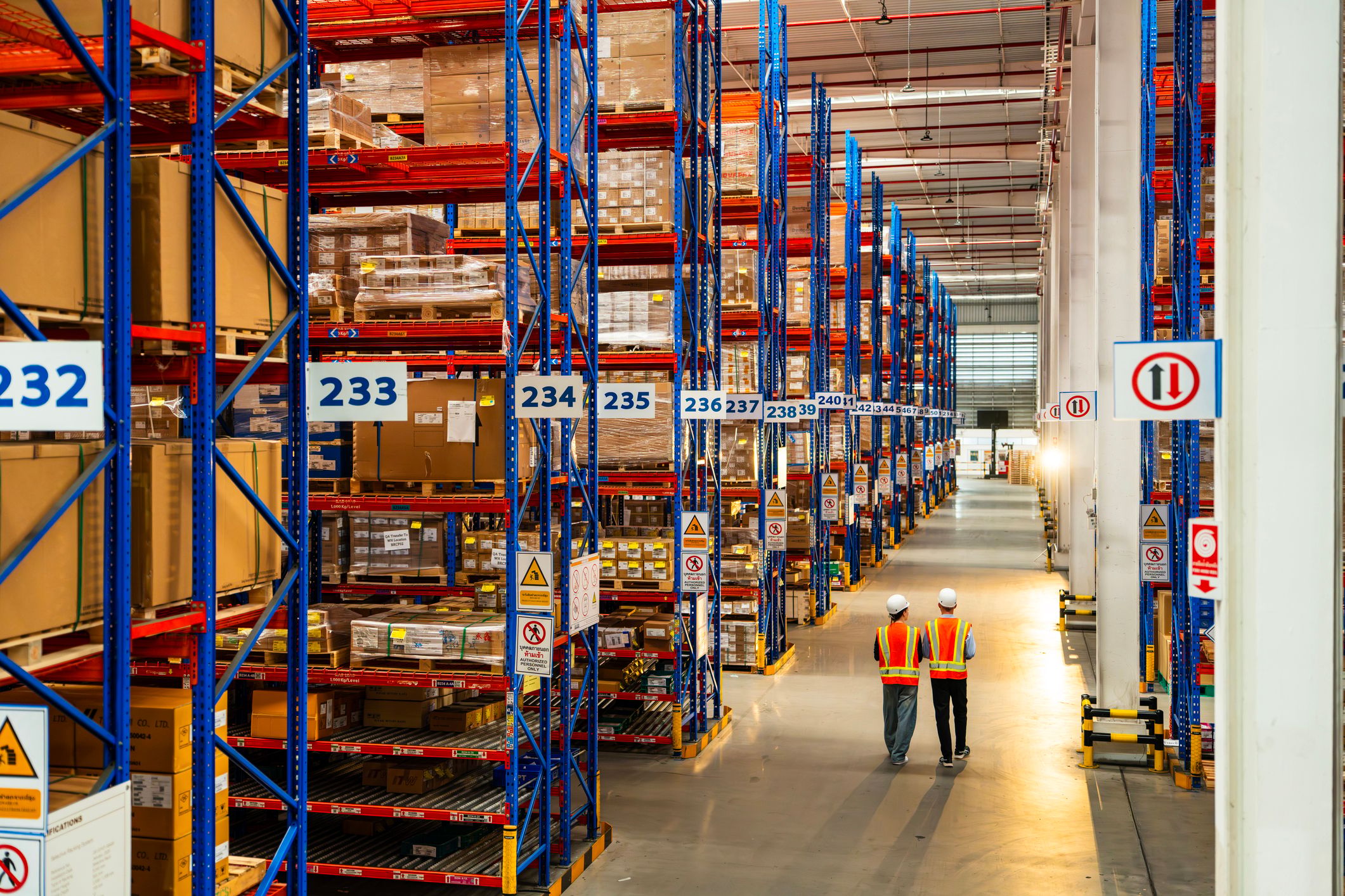 Two warehouse workers walking down an aisle in a large warehouse