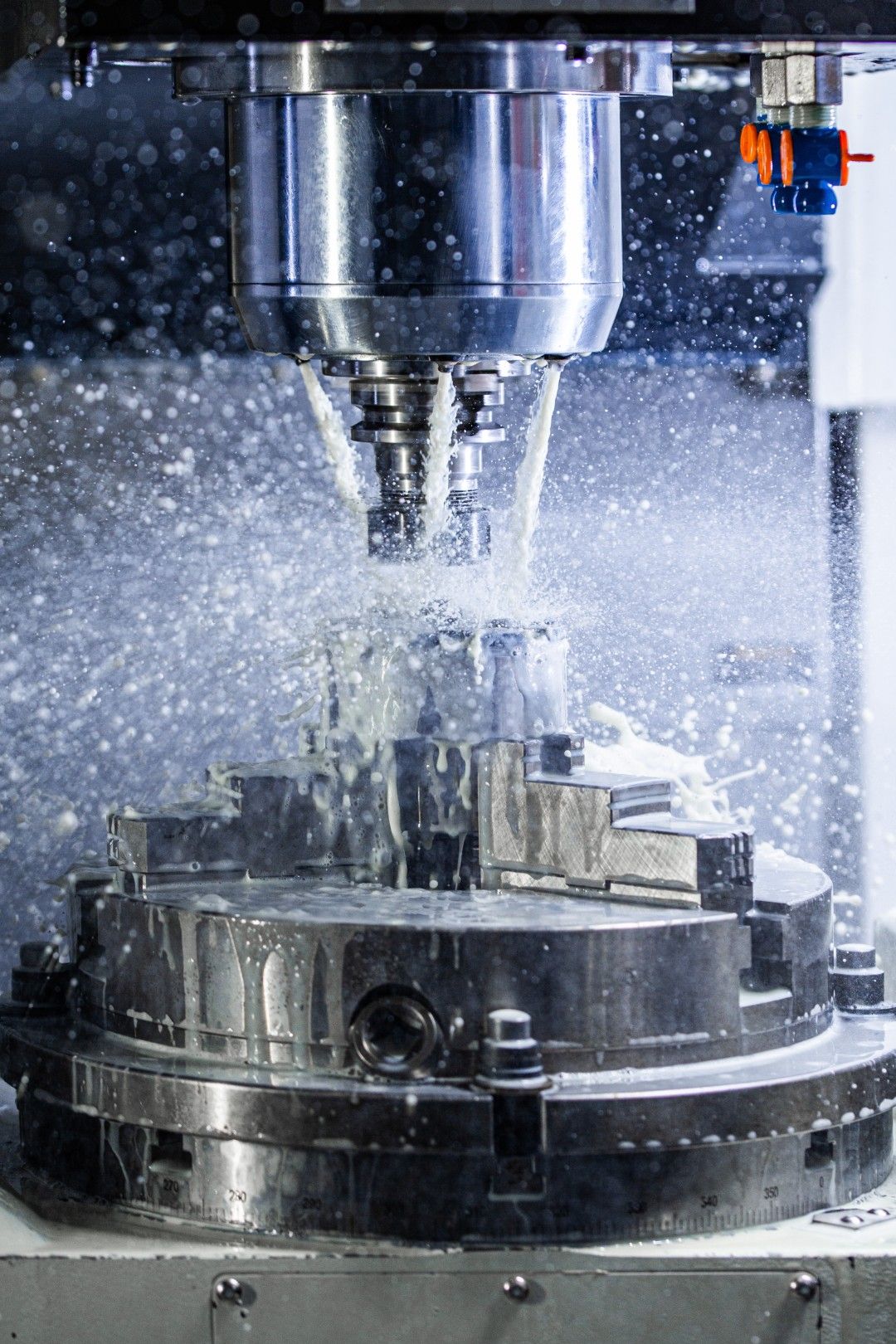 Close-up of a vertical mill cutting a round steel part under a heavy stream of coolant