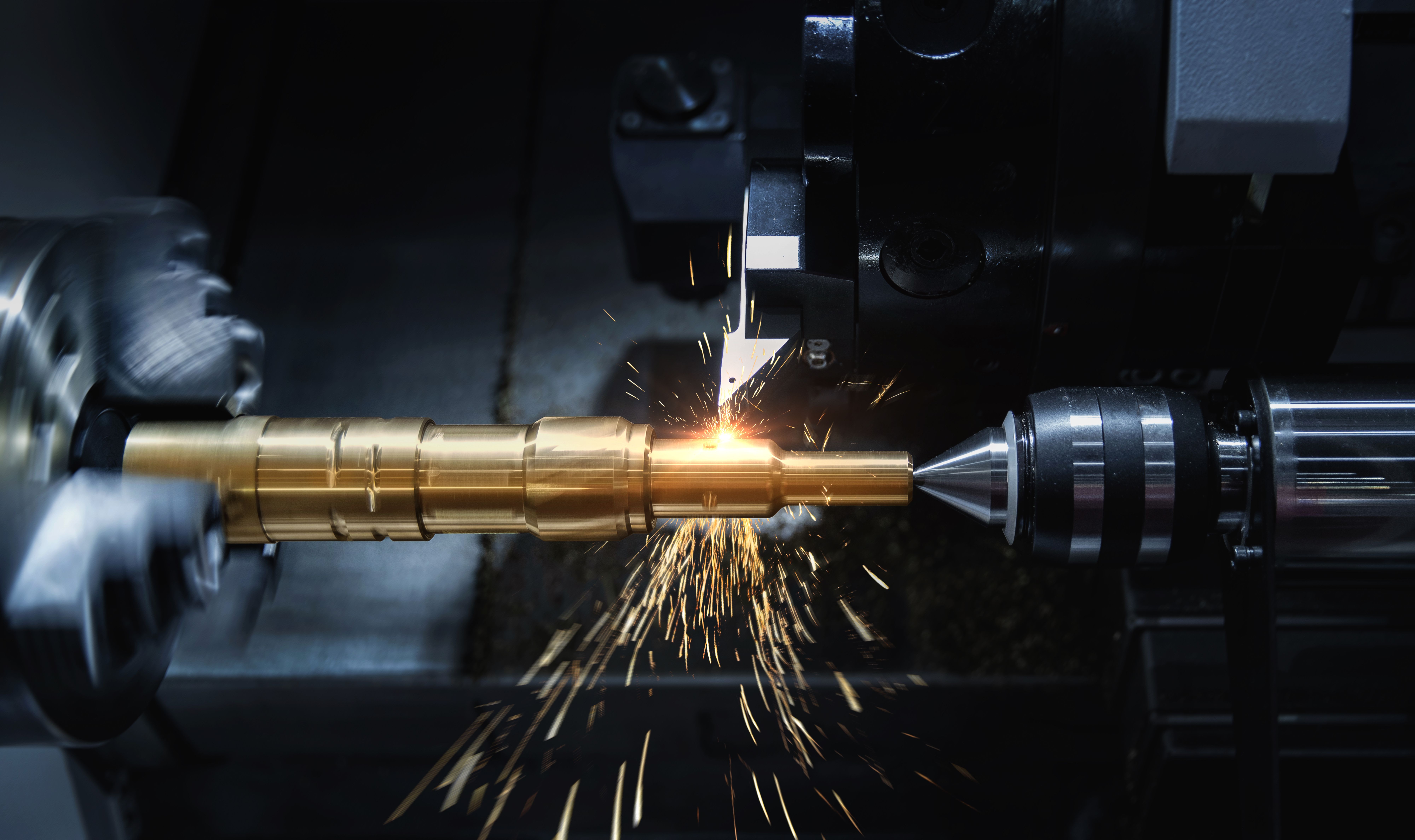 CNC lathe machining a brass shaft, sparks flying from the cutting tool