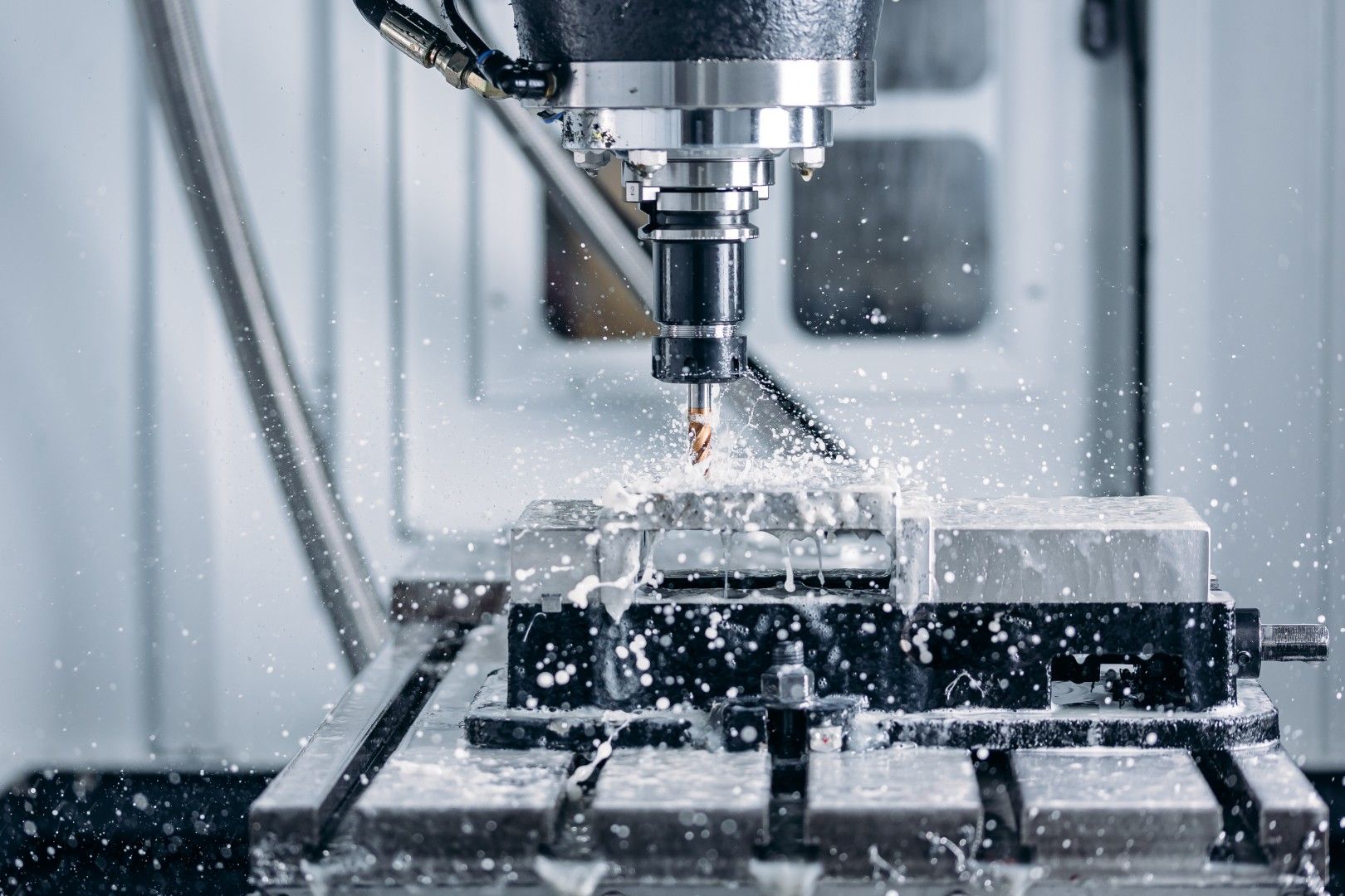 CNC machining center milling a steel block with coolant spraying over the cutter